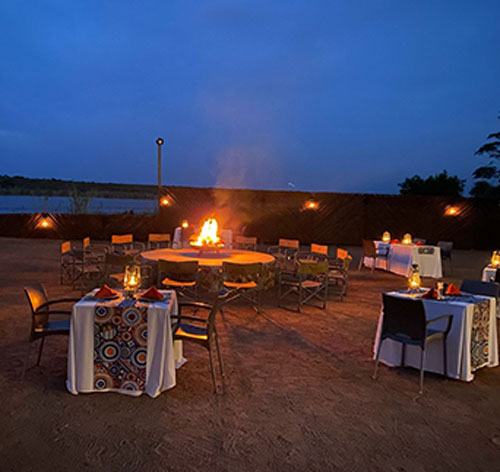 Evening picture of seated dinner area around a bonfire